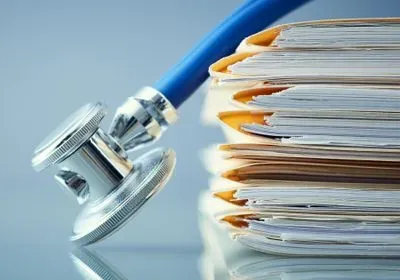 Blue stethoscope resting on a pile of folders filled with papers 